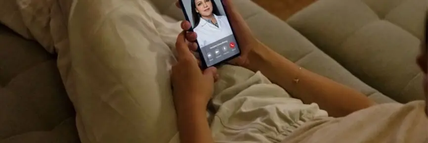 Jente ligger i sofaen og snakker med en lege på facetime på mobilen