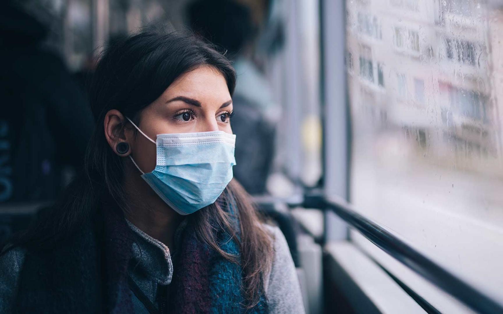 Kvinne på transportmiddel som har på seg munnbind og ser ut av vinduet
