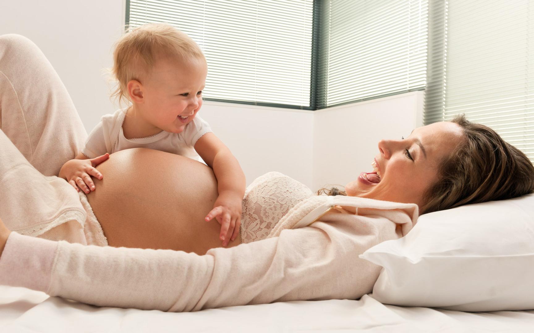 Gravid kvinne med en lite barn som ler i sofaen