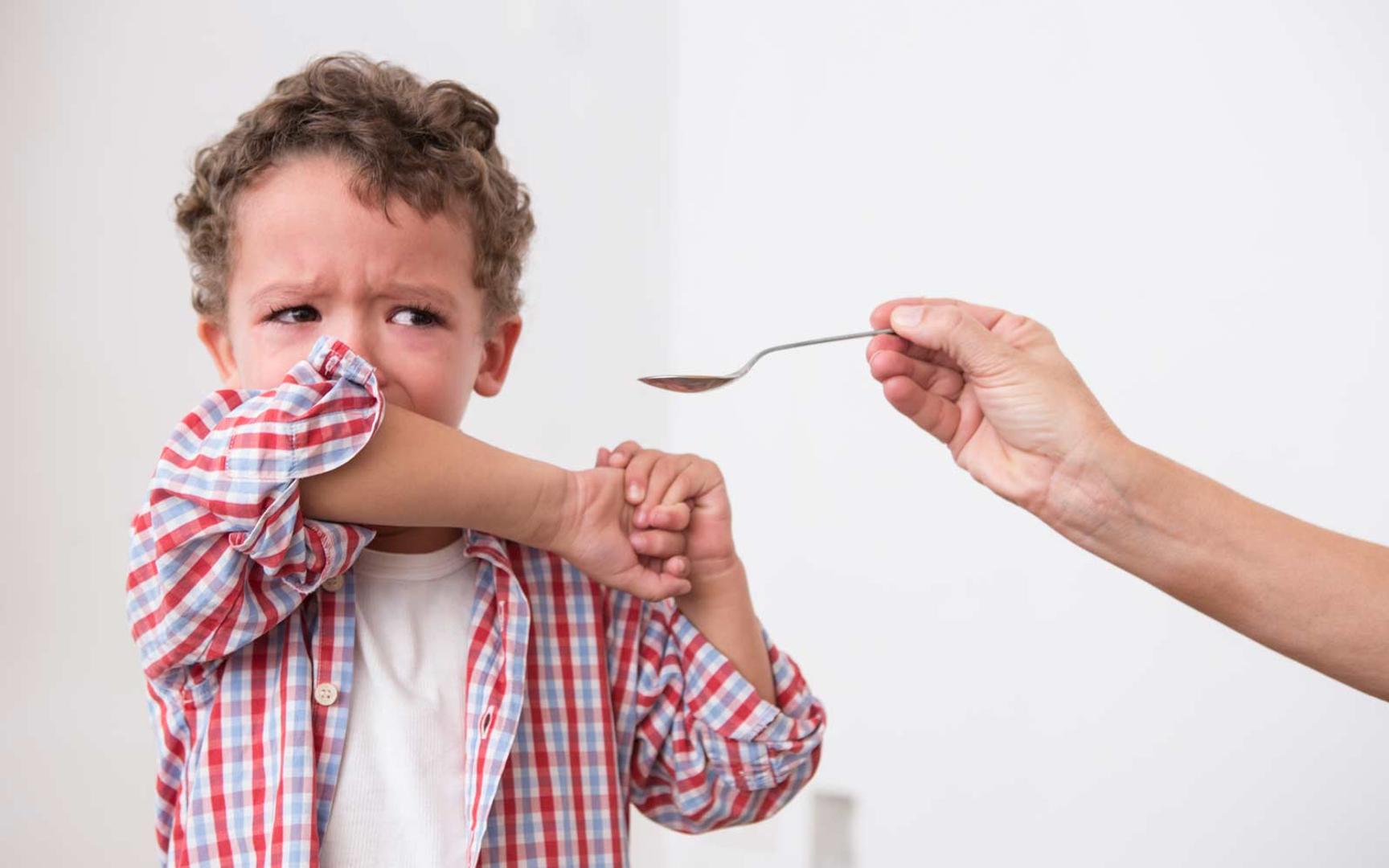Bilde av et barn som får noe på en skje og barnet holder armen foran munnen.