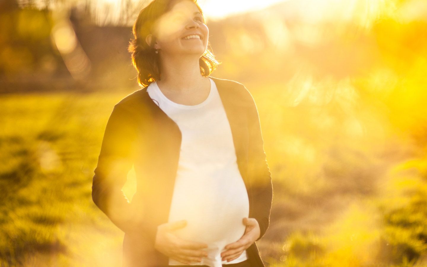 Dame som smiler ute i naturen, mens hun holder på sin gravide mage