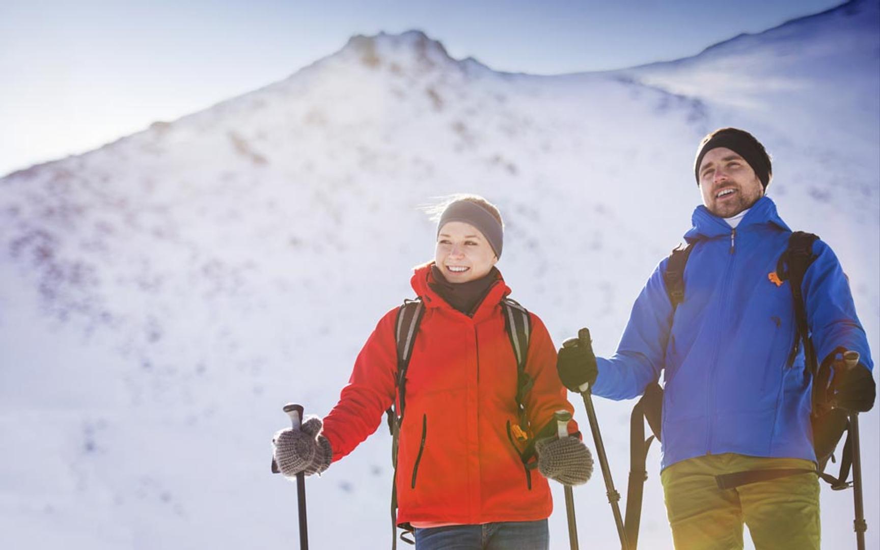 Bilde av en kvinne og en mann som med ski og ryggsekk stående med snødekt fjell i bakgrunnen.