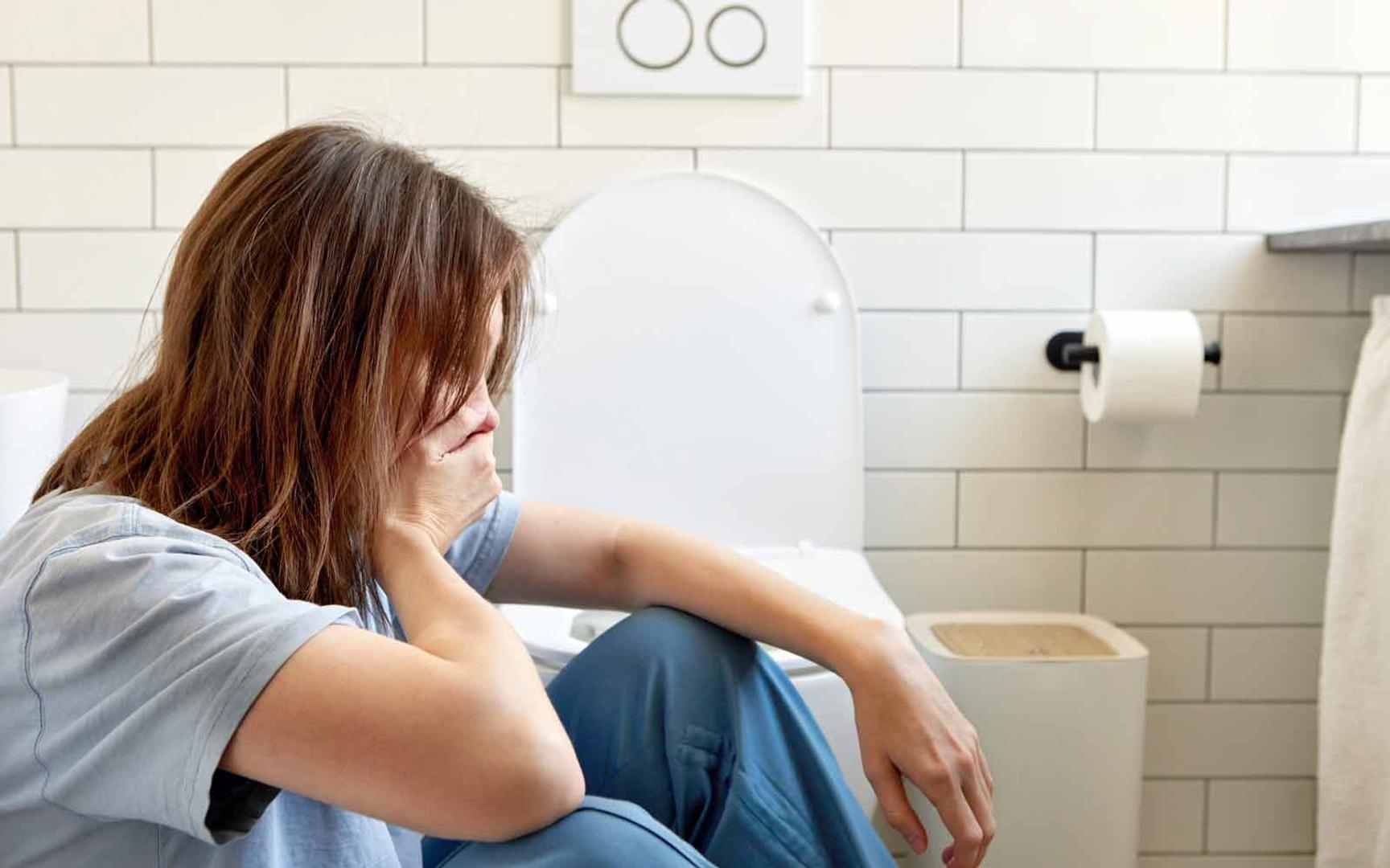 Kvinne sitter på gulvet ved toaletter og holder seg for munnen