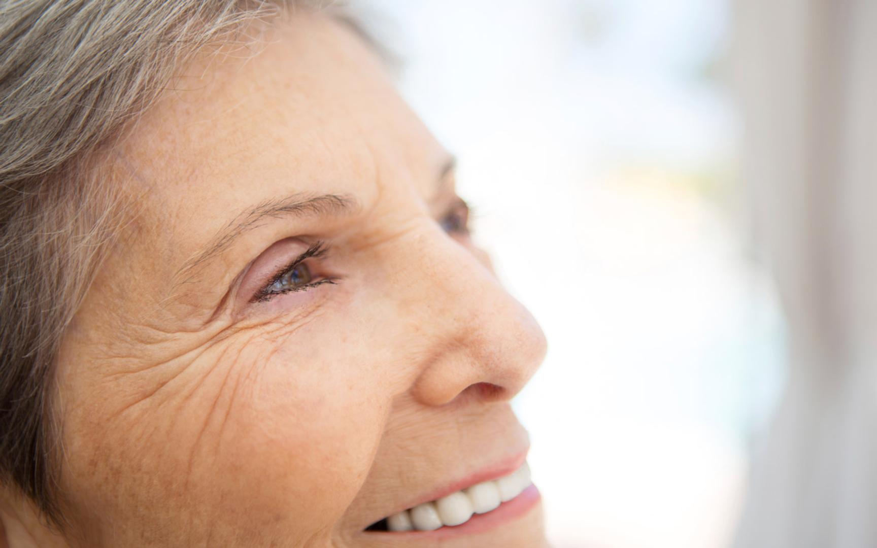 Nært bilde av ansikt til en eldre dame som ser utover og smiler