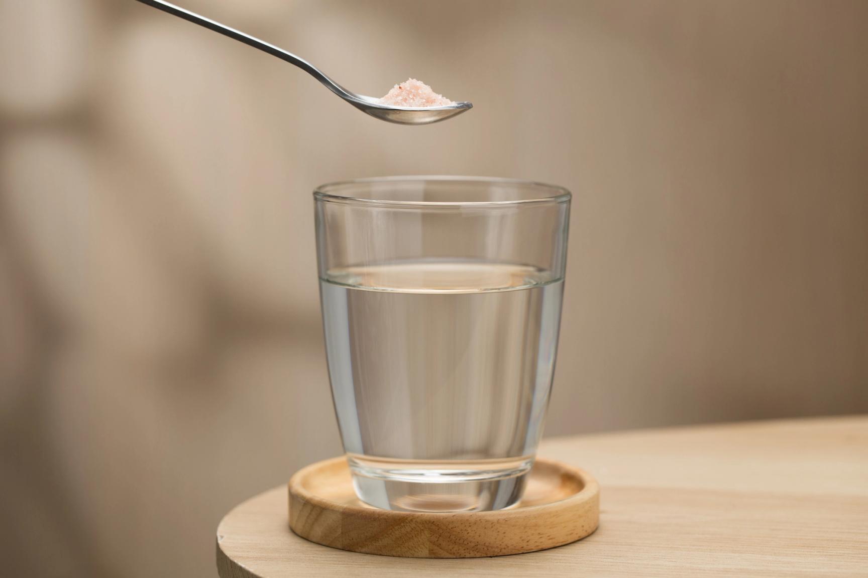 En teskje med salter holdes over et glass med vann
