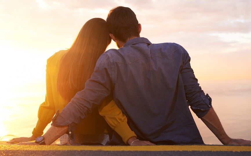 Et par sitter sammen med hodene mot hverandre i et gyllent lys