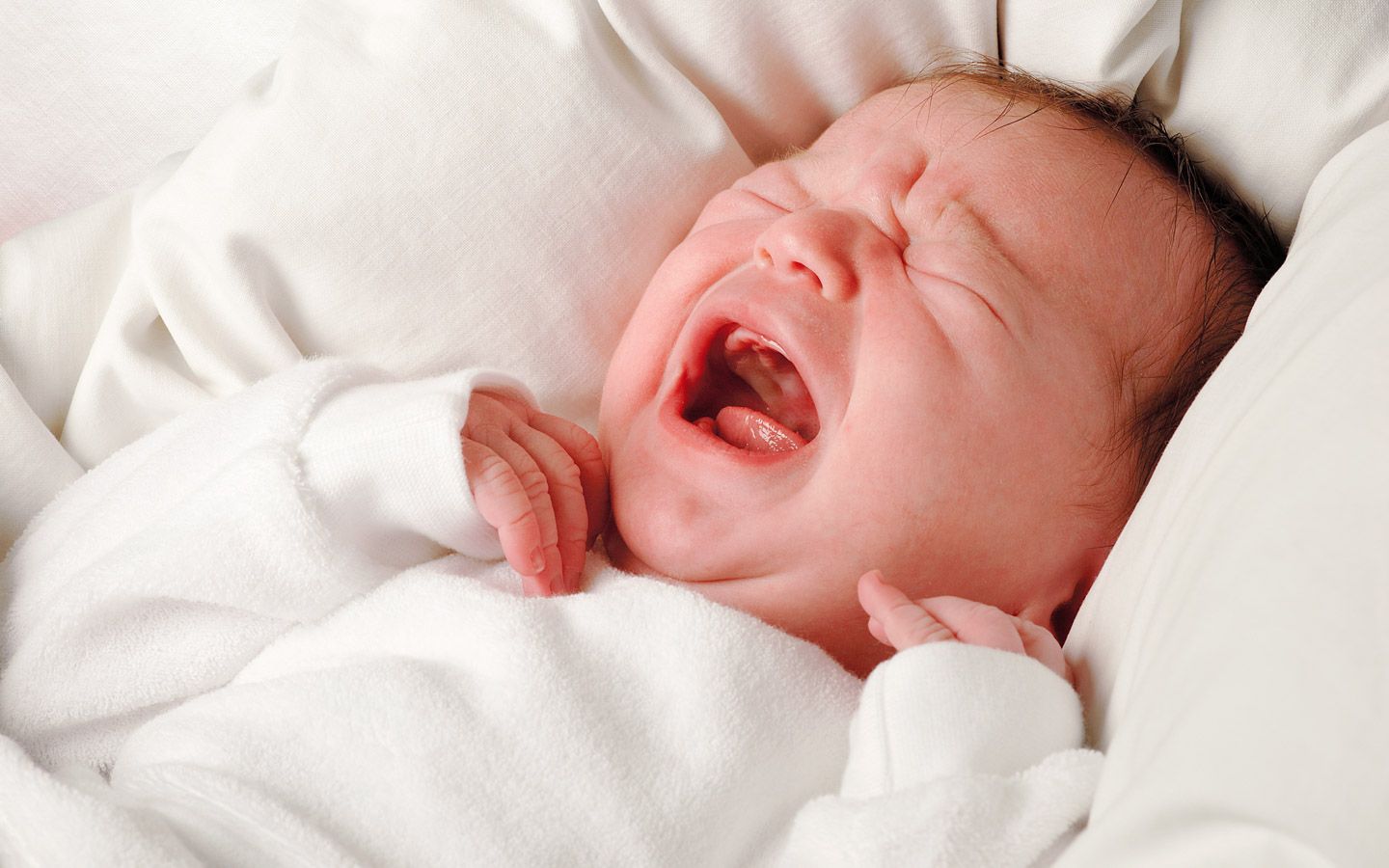 En baby som gråter liggende i en seng. 