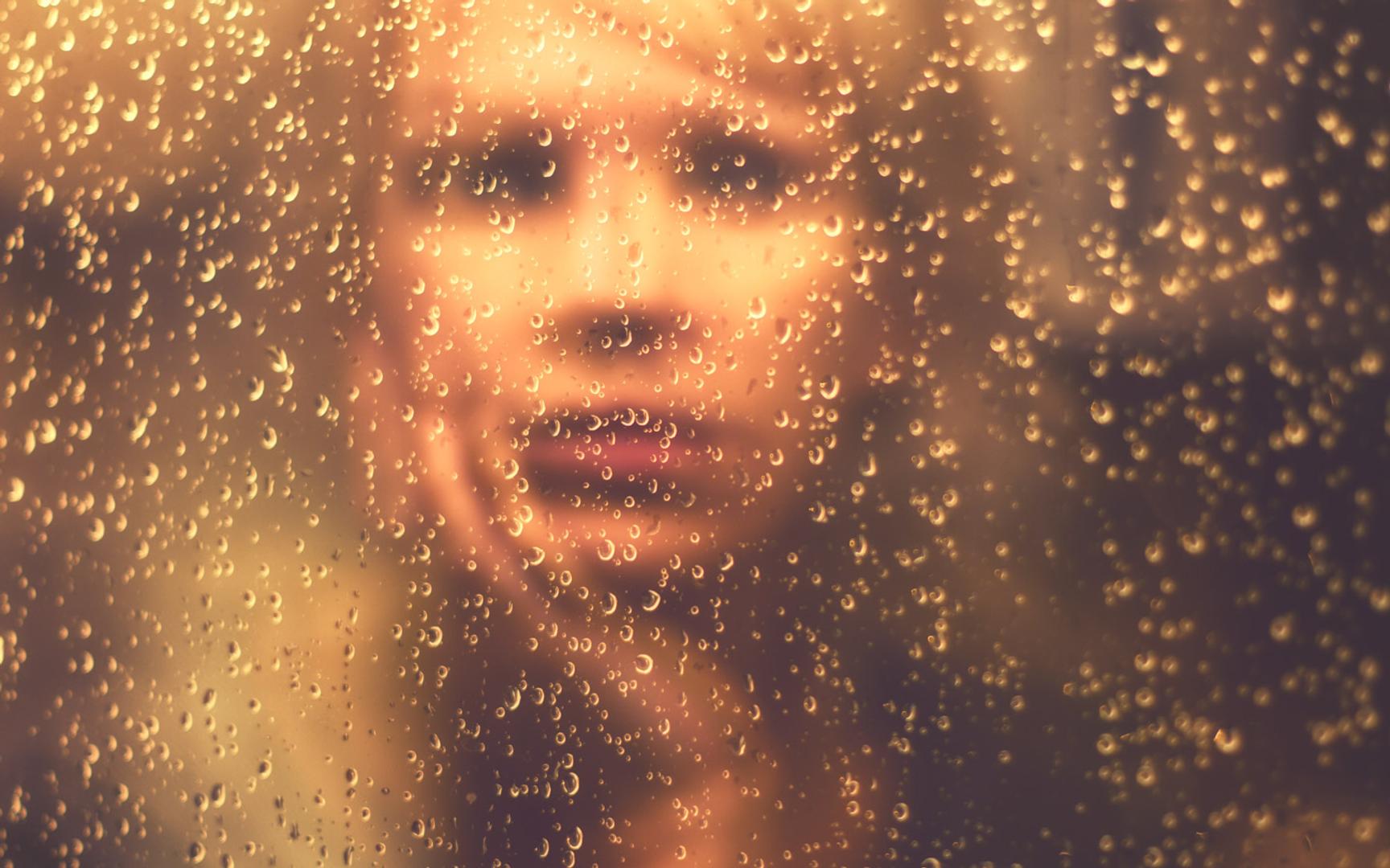 Bilde av en dame som sitter bak en vindu med vanndråper.