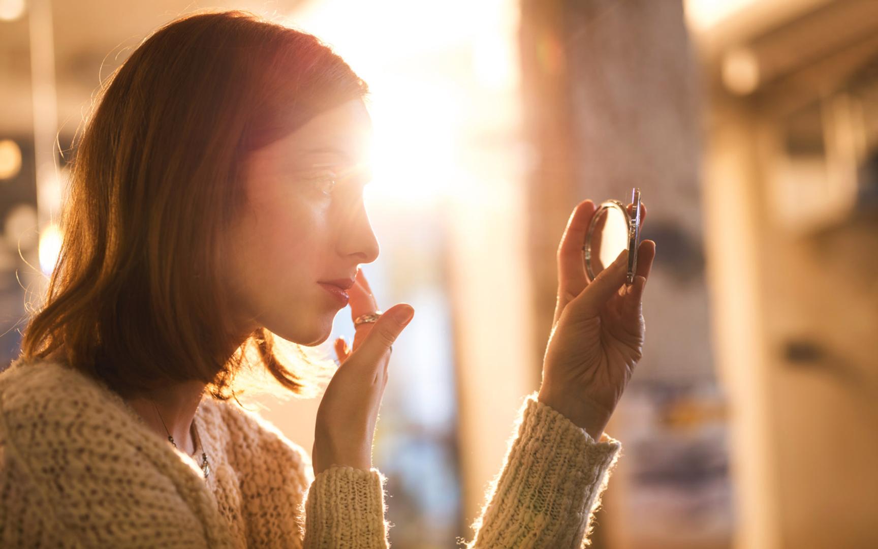 Nærbilde av en dame som fikser på sminken sin mens hun holder opp et lite lommespeil