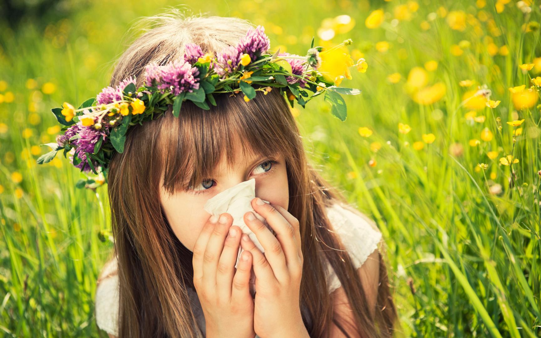 Bilde av en jente som snyter seg sittende i en blomstereng med blomsterkrans i håret.