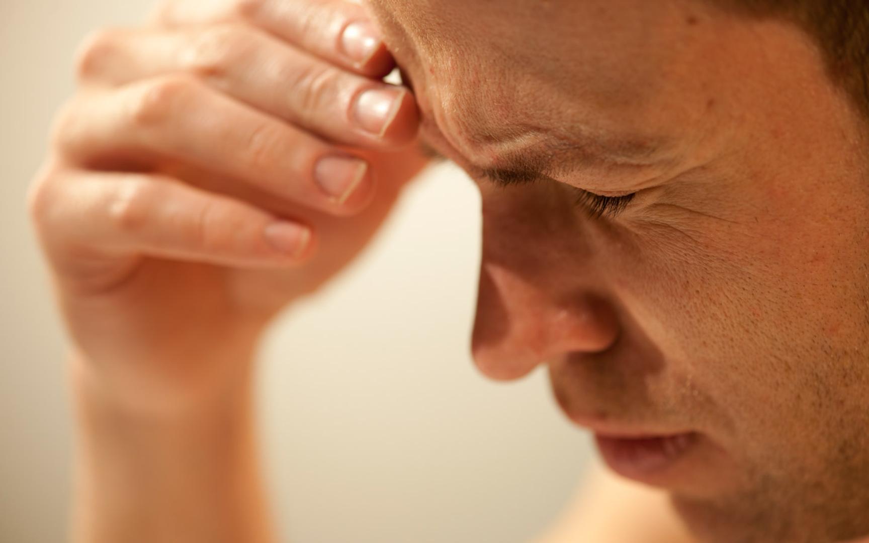 Nærbilde av en mann som holder lukkede øyne og hånden til pannen.