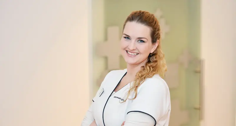 Farmasøyt i uniform smiler og ser i kamera med armene i kors