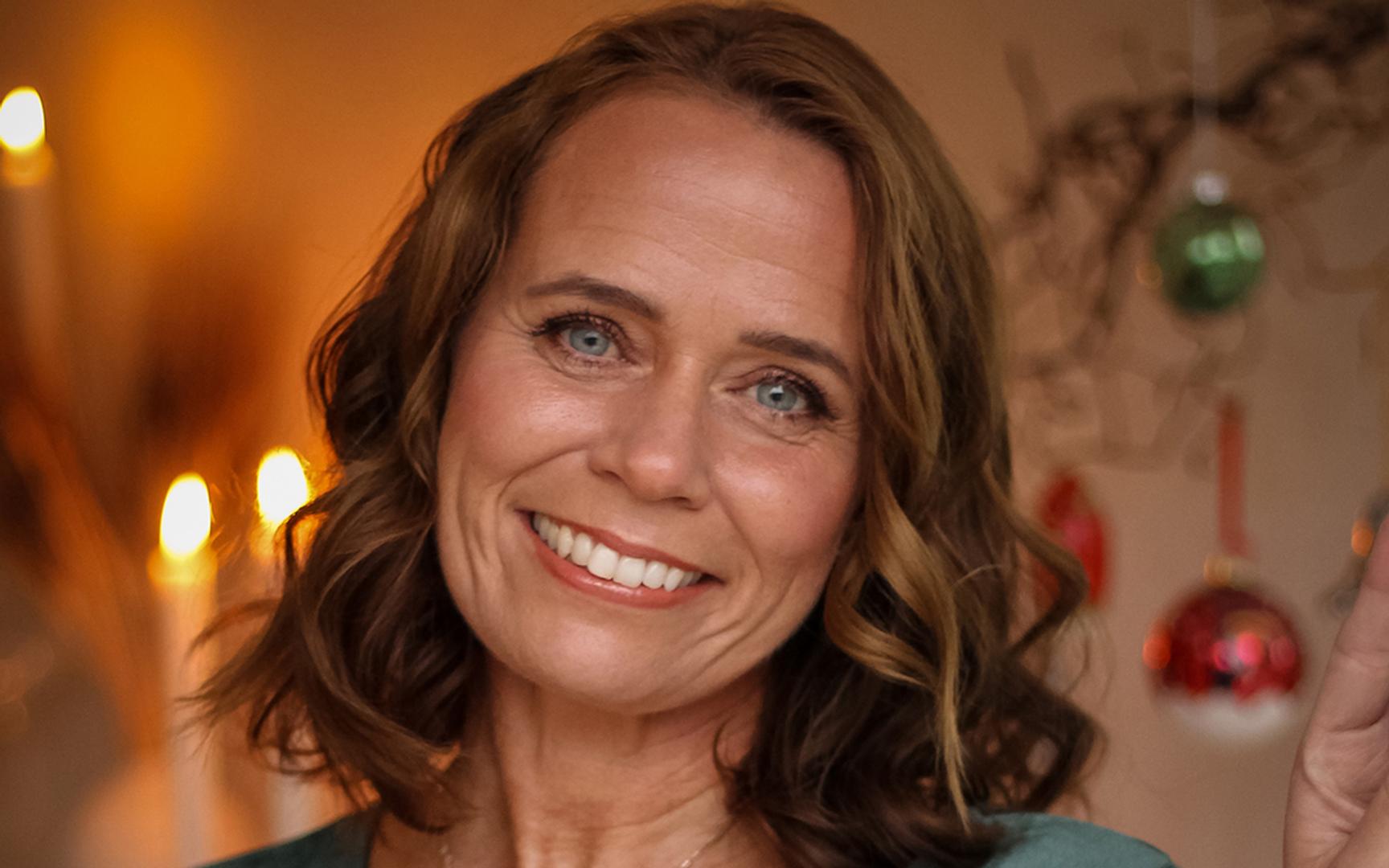 Bilde av en smilende dame med julepynt i bakgrunnen
