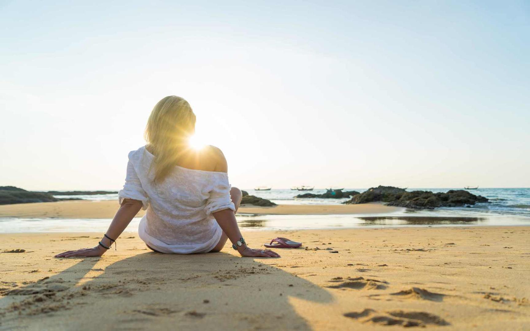 Kvinne som sitter i solen på stranden