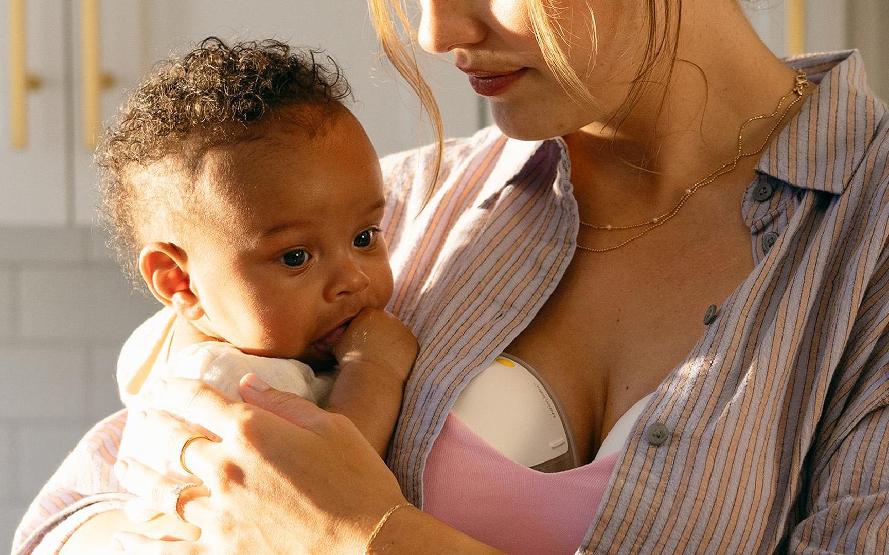 En kvinne med dobbel håndfri brystpumpe holder en baby i armene