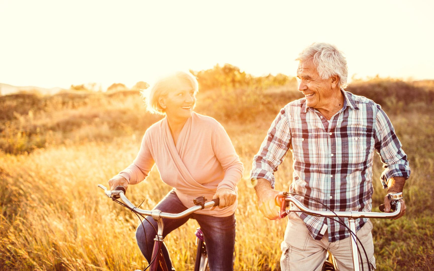 Eldre kvinne og mann som sykler ute i naturlandskap i solnedgang