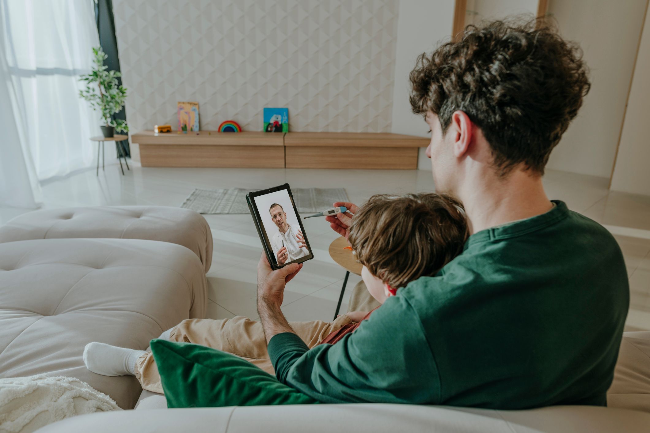 En far sitter med en sønn i fanget og har en videosamtale med en lege