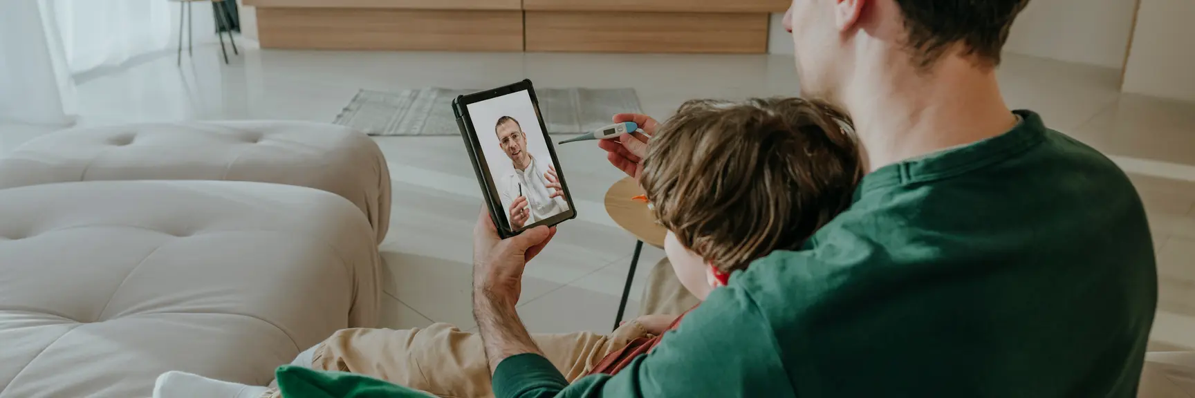 En far sitter med en sønn i fanget og har en videosamtale med en lege