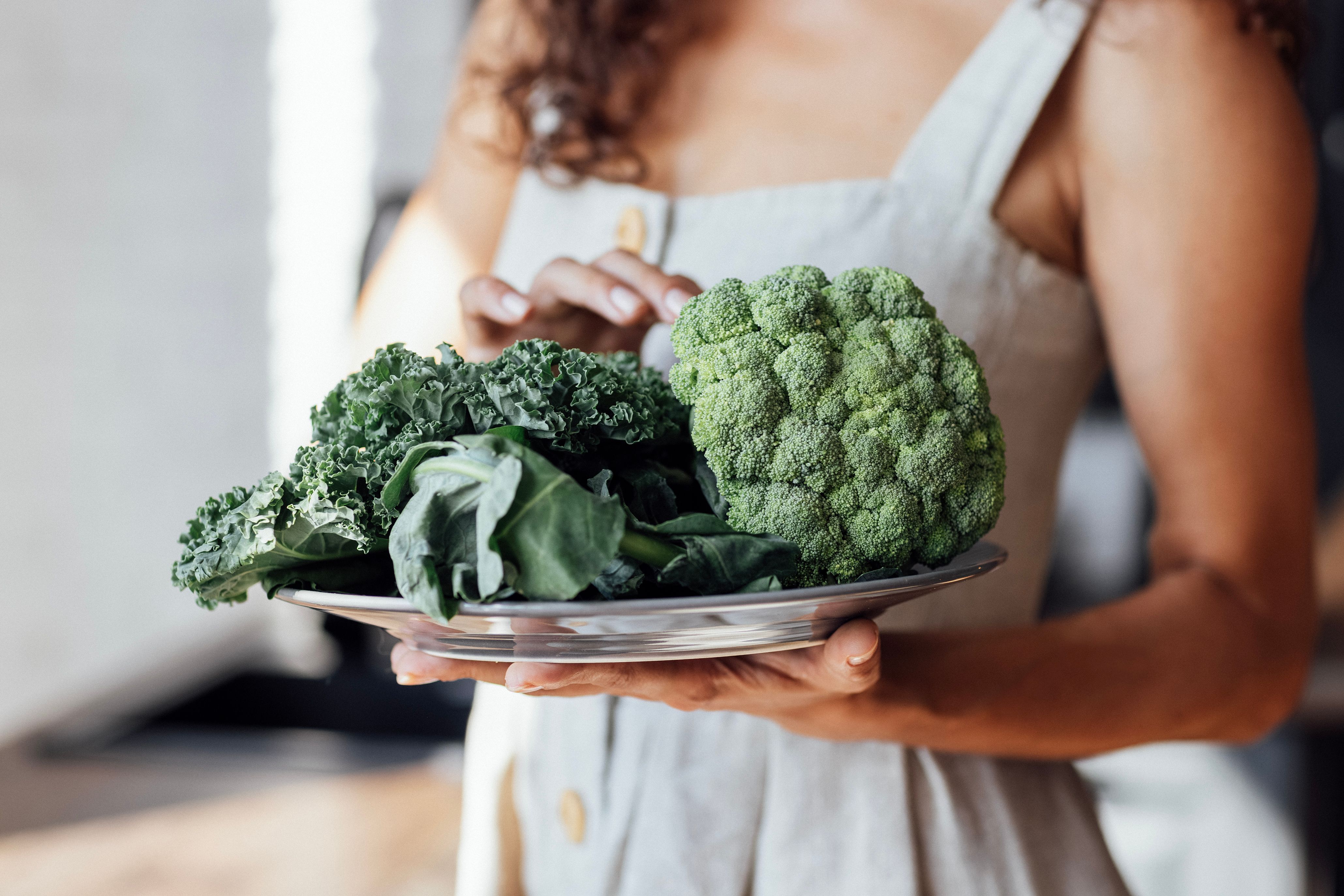 En kvinne holder et fat med ulik grønnsaker.