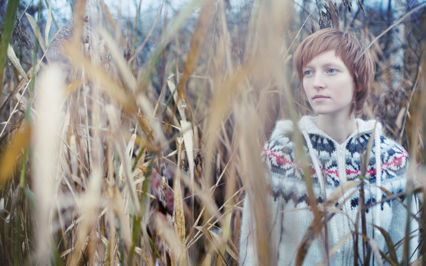 Bilde av en dame som står blant høye strå. 