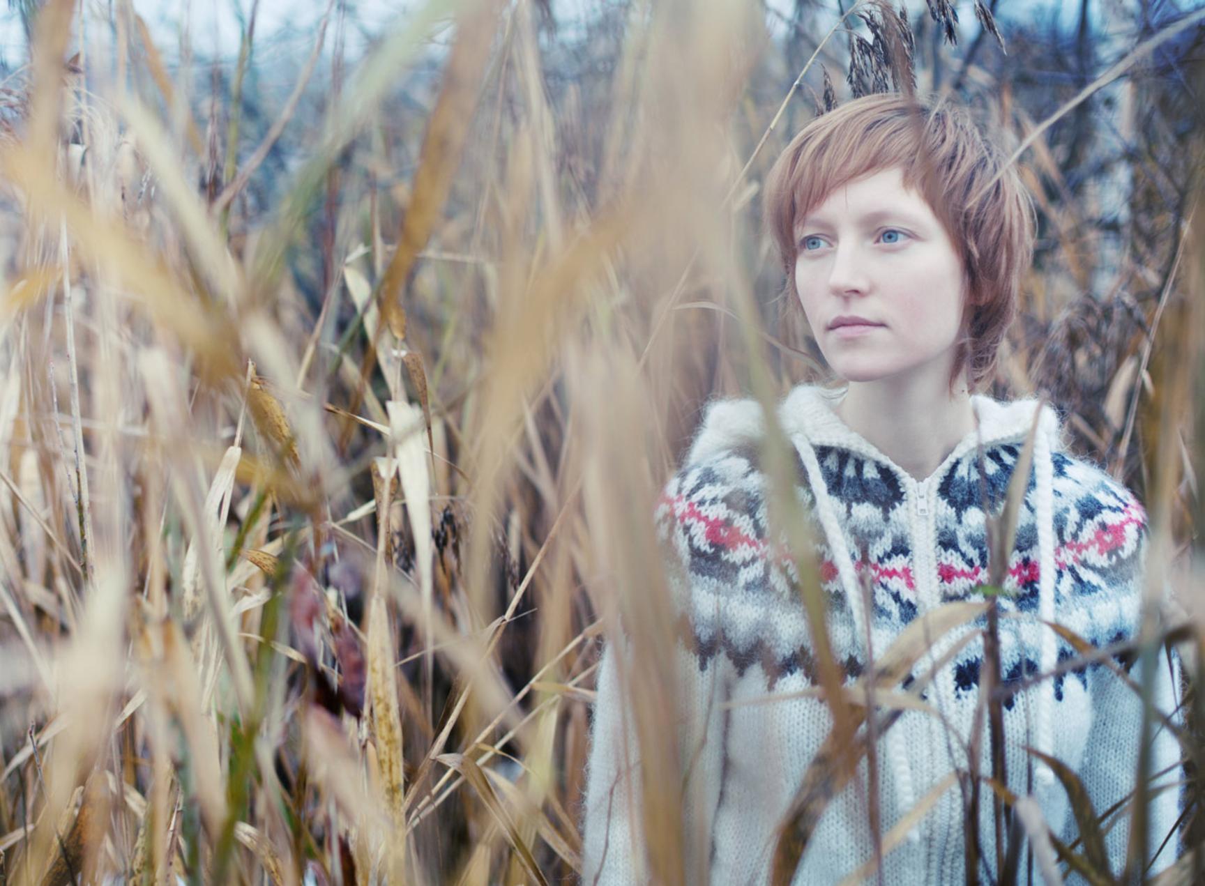 Bilde av en dame som står blant høye strå.