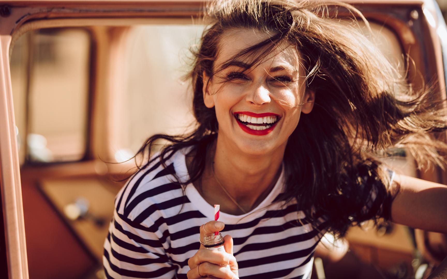 En kvinne i stripete genser går ut av en bil og smiler mot kameraet