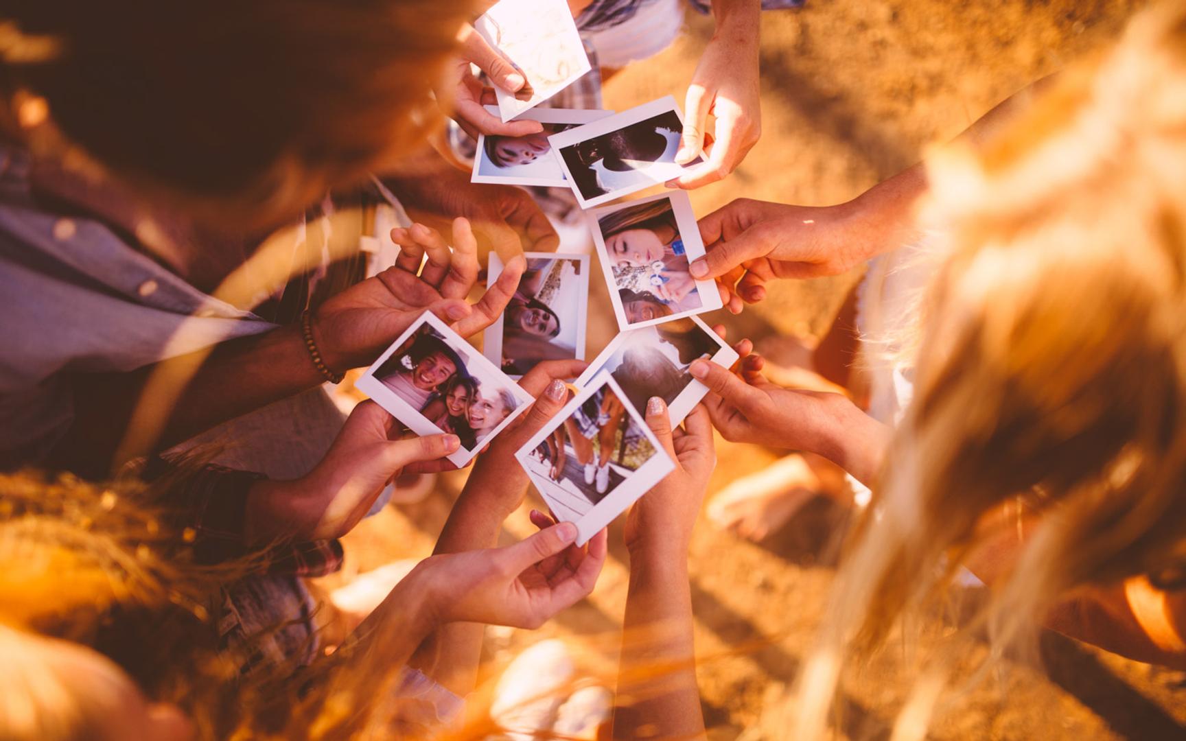 Bilde ovenfra hvor flere mennesker holder frem hendene og viser frem polaroid bilder.