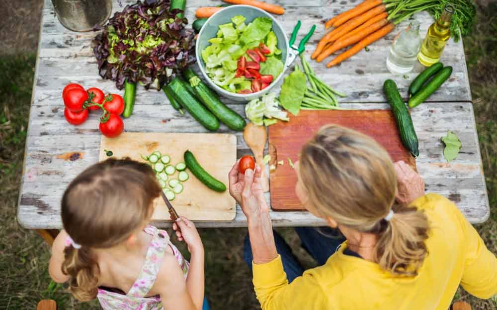 Bilde tatt ovenfra av en dame og et barn som sitter ved et bord fullt av grønnsaker 