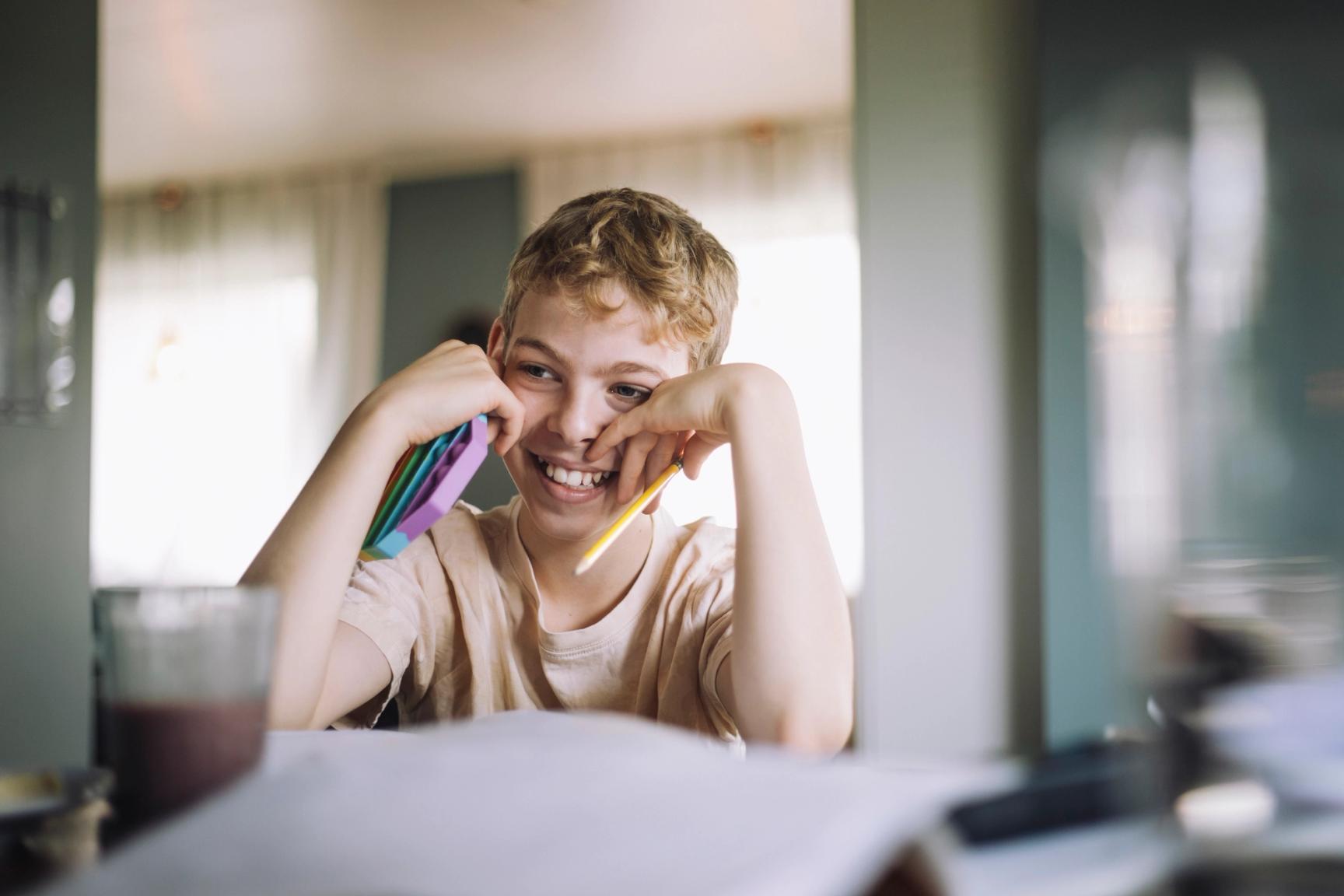 Gutt sitter ved et bord med en blyant og en pop it leke i hendene