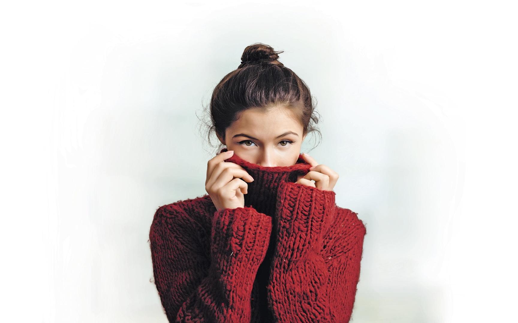 Kvinne med rød genser som delvis skjuler ansiktet med kragen