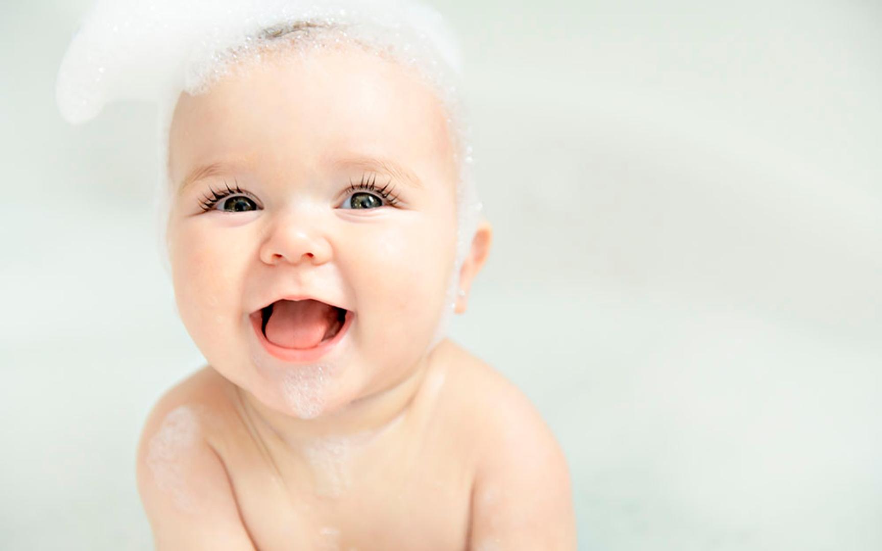 Nærbilde av en smilende baby i badekaret med såpeskum på hodet