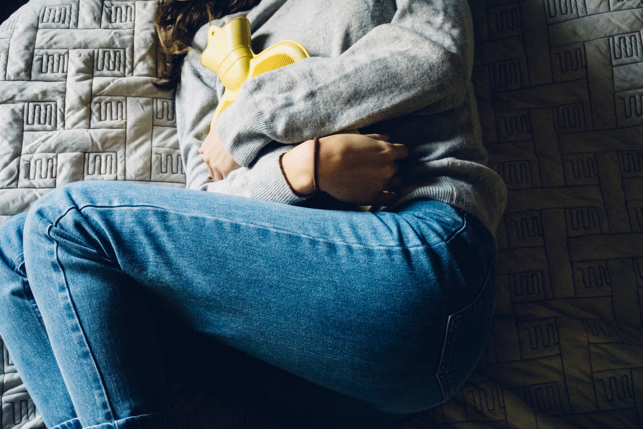 Kvinne ligger i seng med varmeflaske på magen