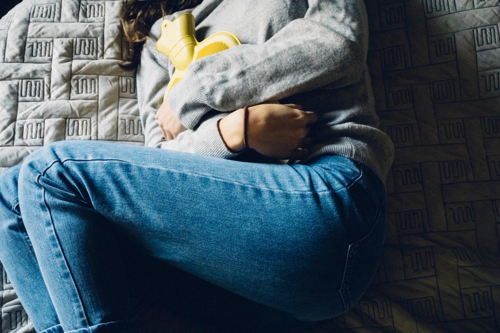 Kvinne ligger i seng med varmeflaske på magen