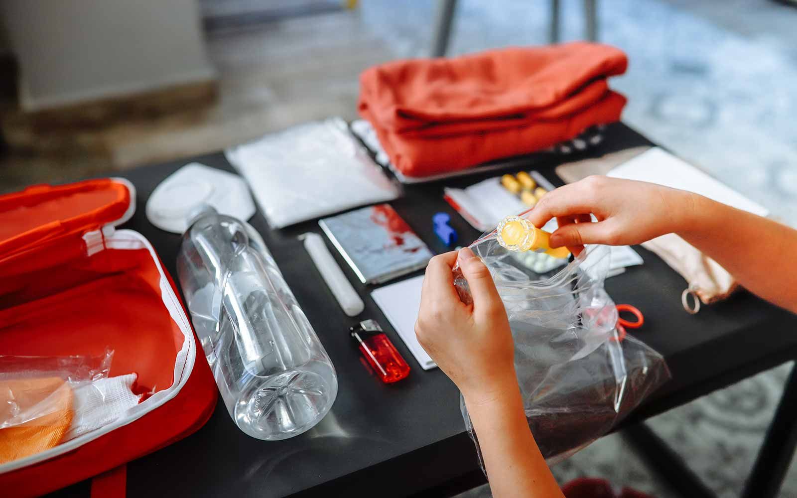 Person som sitter ved et bord og gjør klart beredskapslager. På bordet ligger blant annet førstehjelpsutstyr, stearinlys, vannflaske og medisiner.