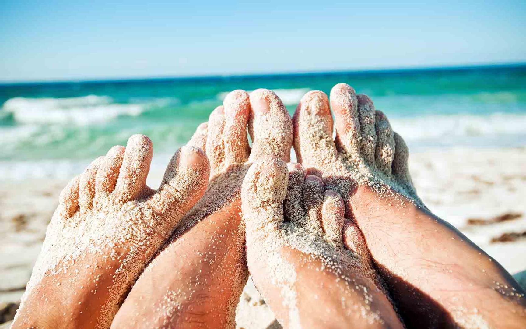 To par føtter delvis dekket med sand på en sandstrand