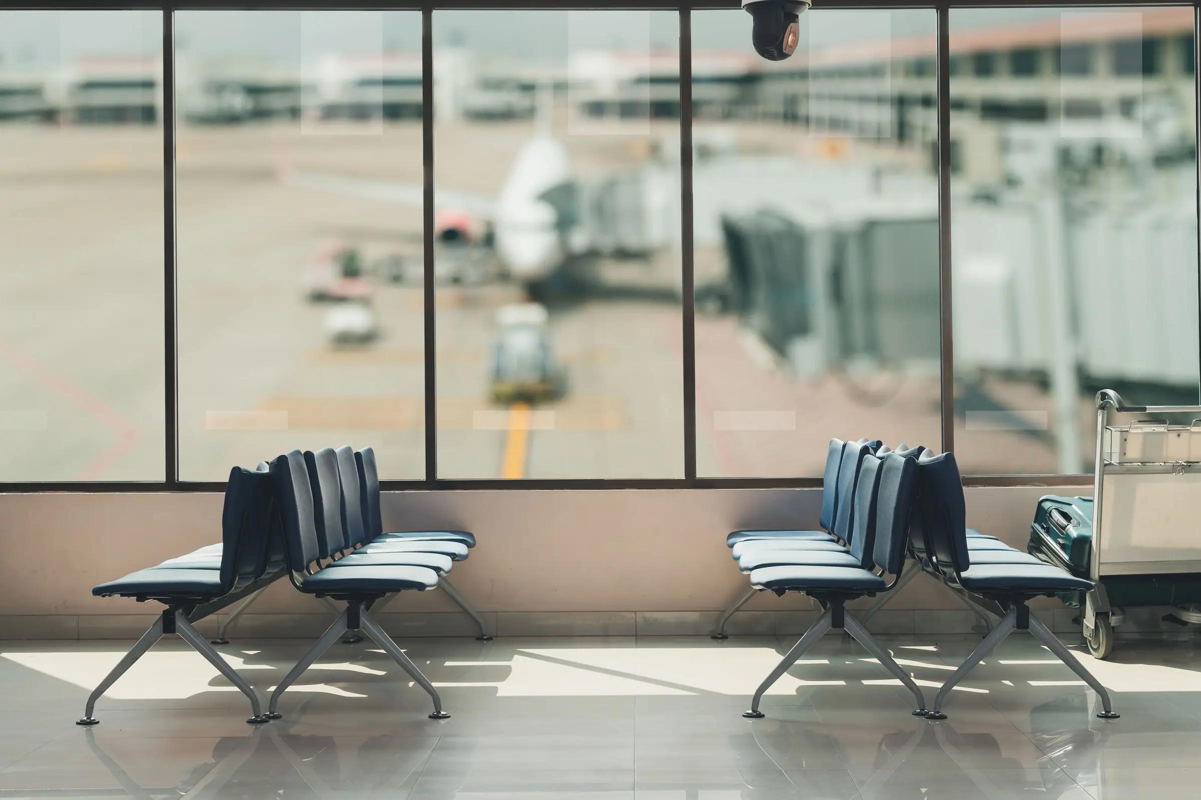 Ventesone på en flyplass, med tomme seter og et fly som lastes i bakgrunnen