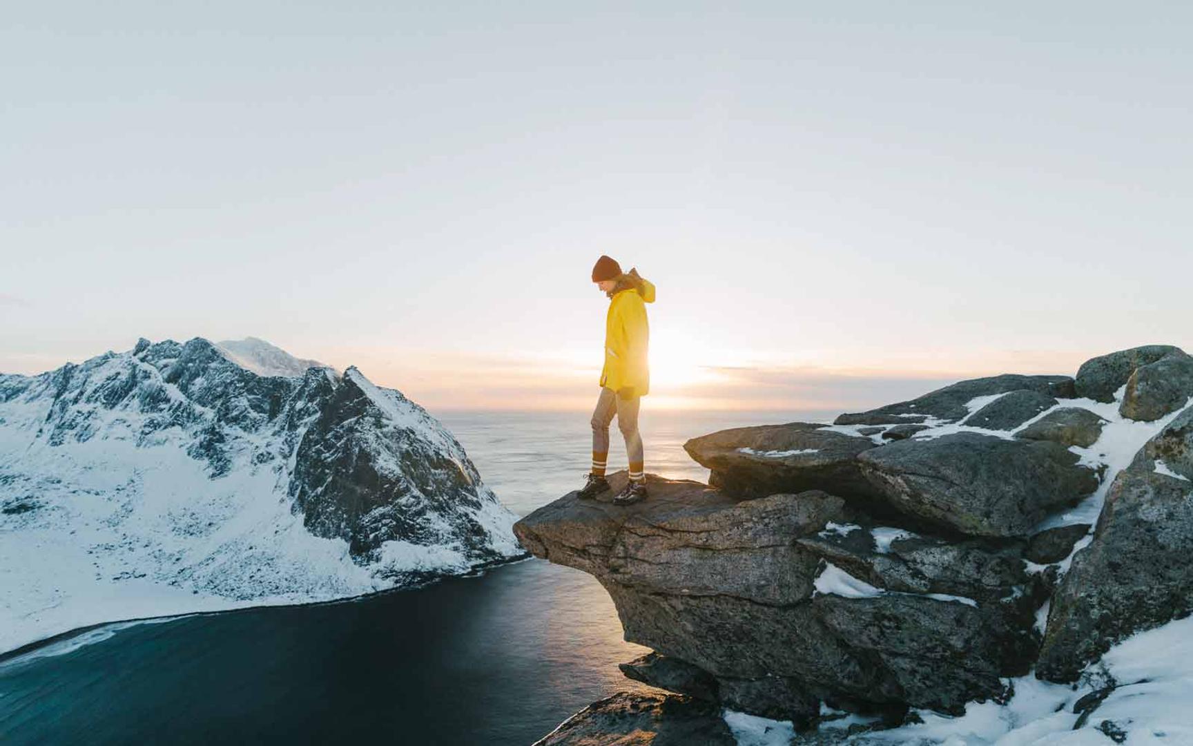 En kvinne står på en klippe og ser utover snødekte fjell og sjø