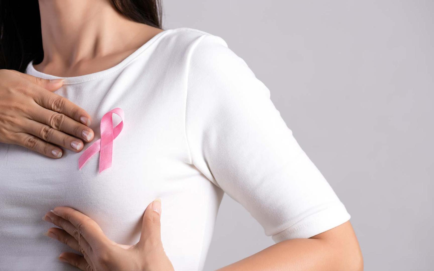 En kvinne med hvit t-skjorte og rosasløyfe undersøker brystene