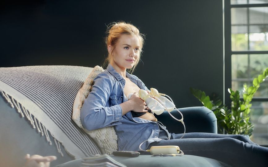 En dame sittende i en sofa og benytter dobbel brystpumpe. 