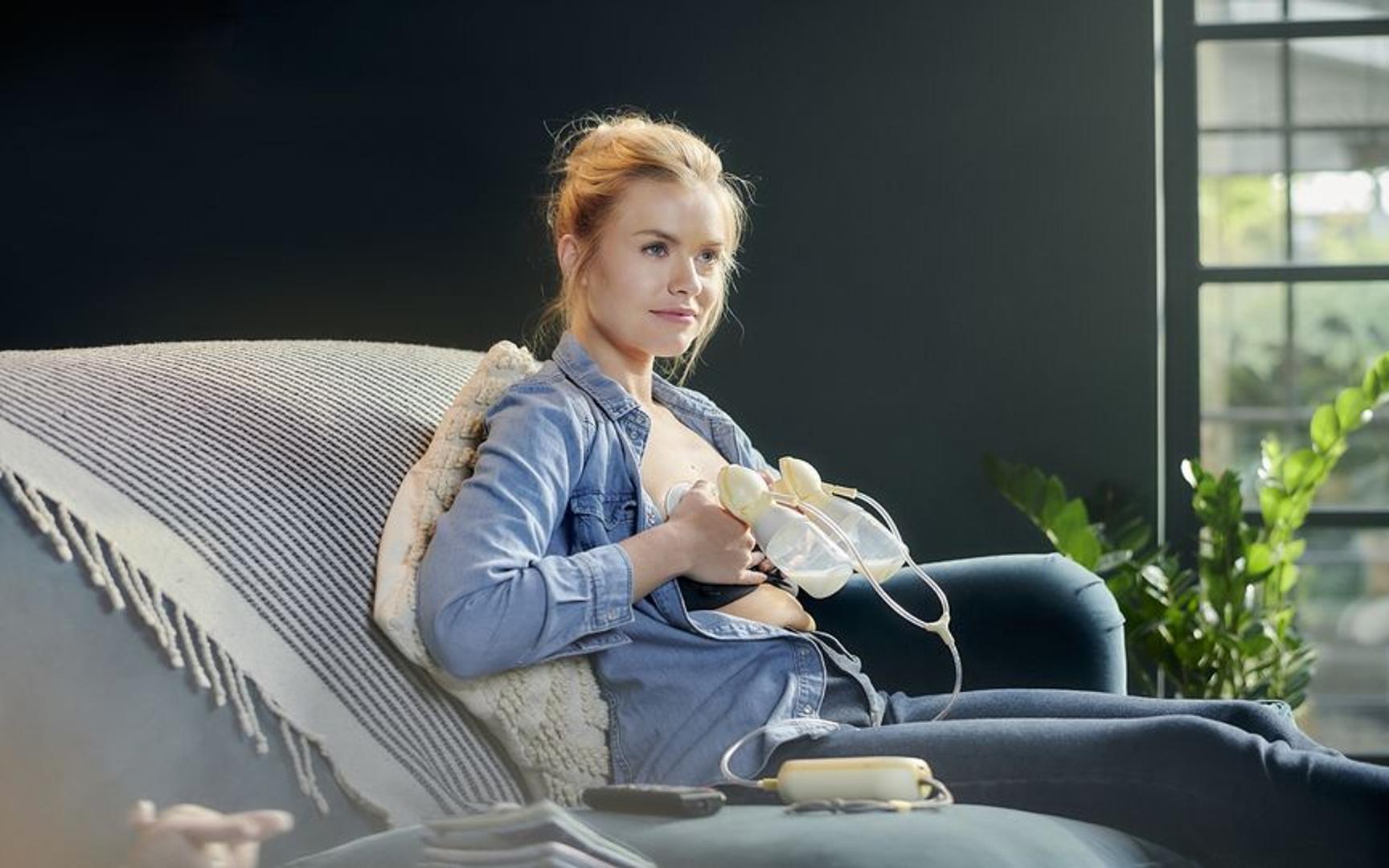 En dame sittende i en sofa og benytter dobbel brystpumpe.
