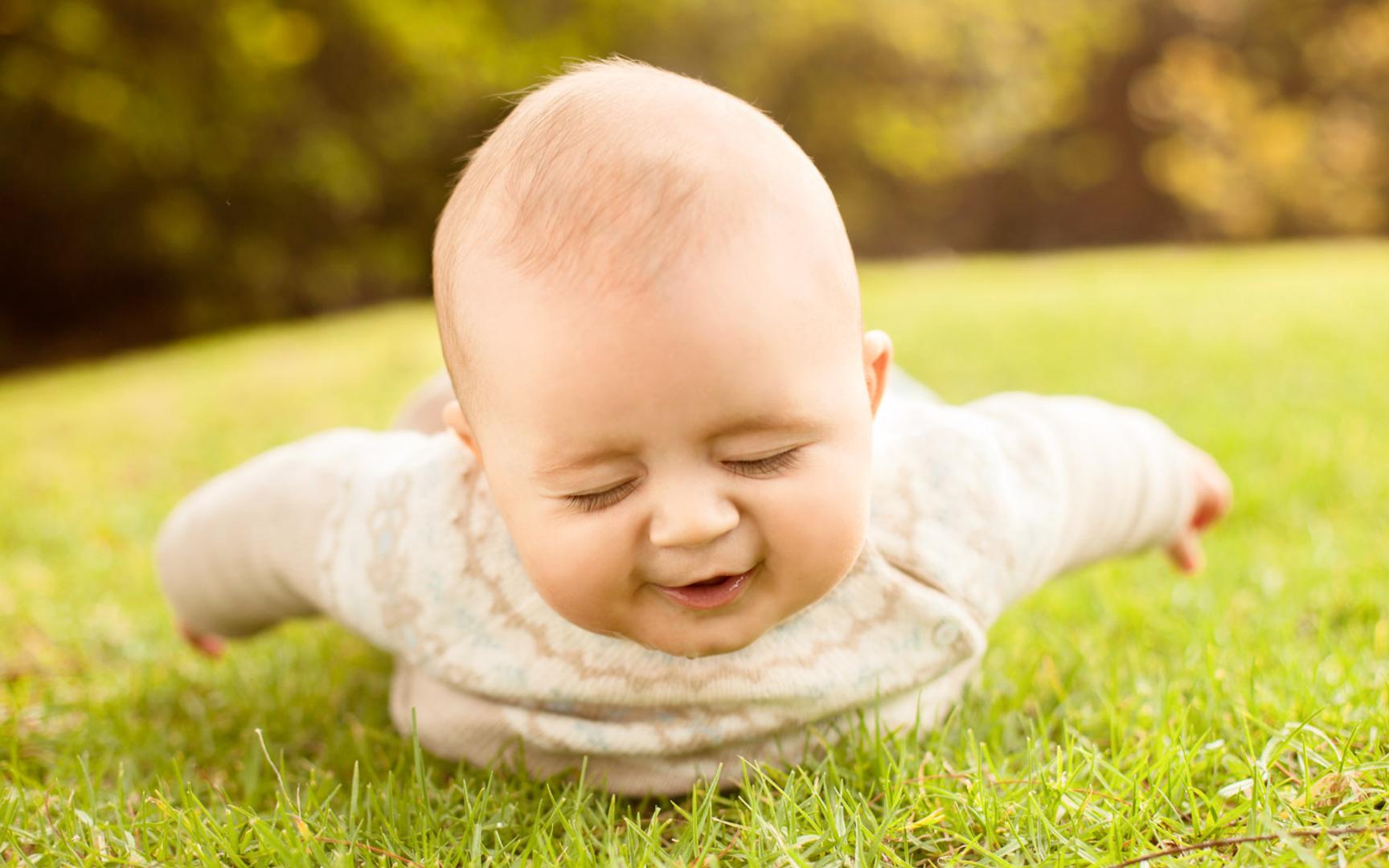 En smilende baby som ligger på magen i gresset