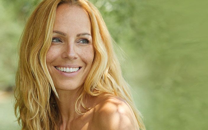 Ung kvinne med langt lyst hår som smiler og ser seg over naken skulder