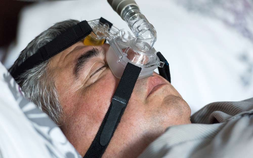 Eldre mann som sover på rygg med pustemaske over nesen