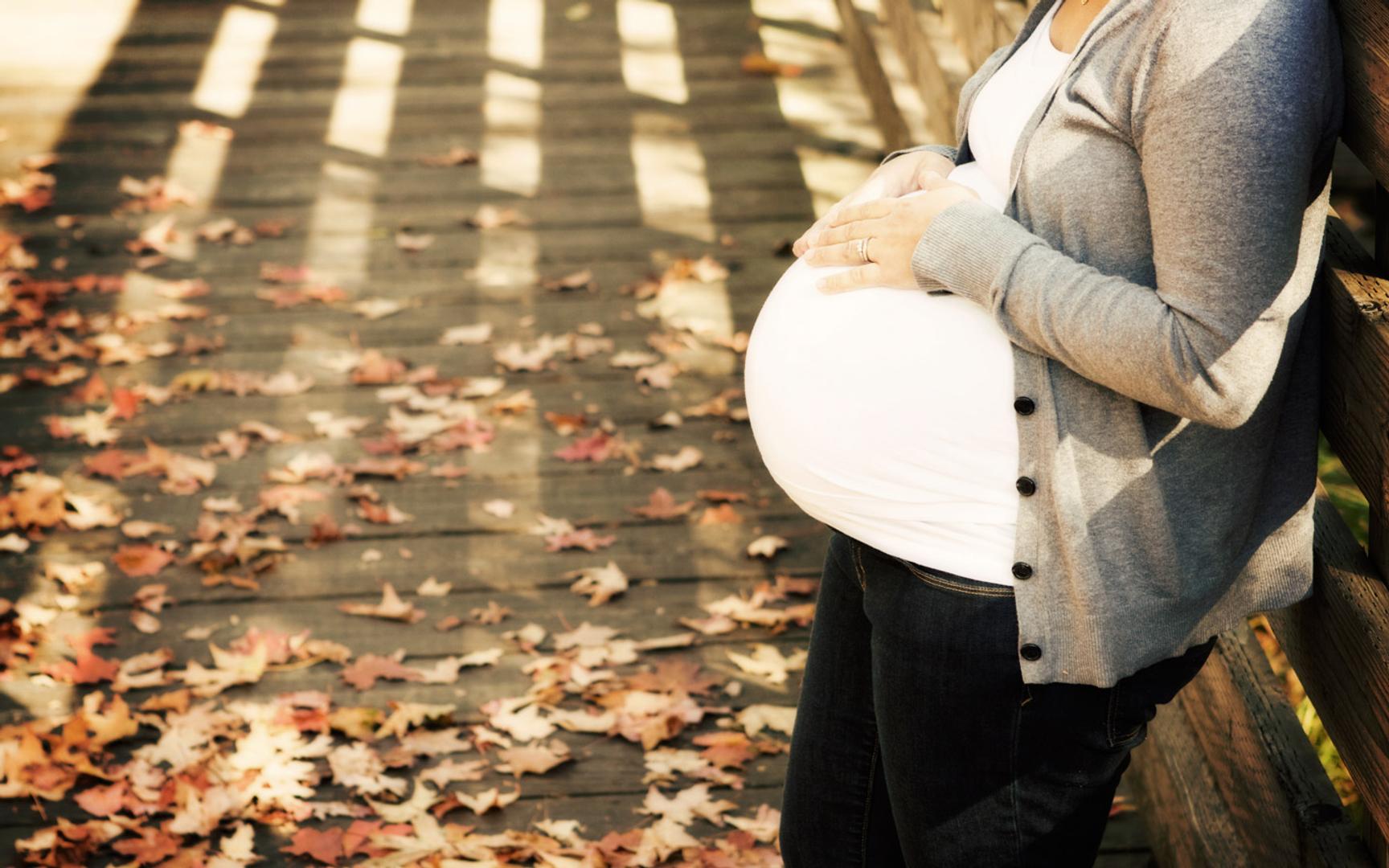 En gravid person som lener seg mot et gjerde og holder begge hendene på magen.