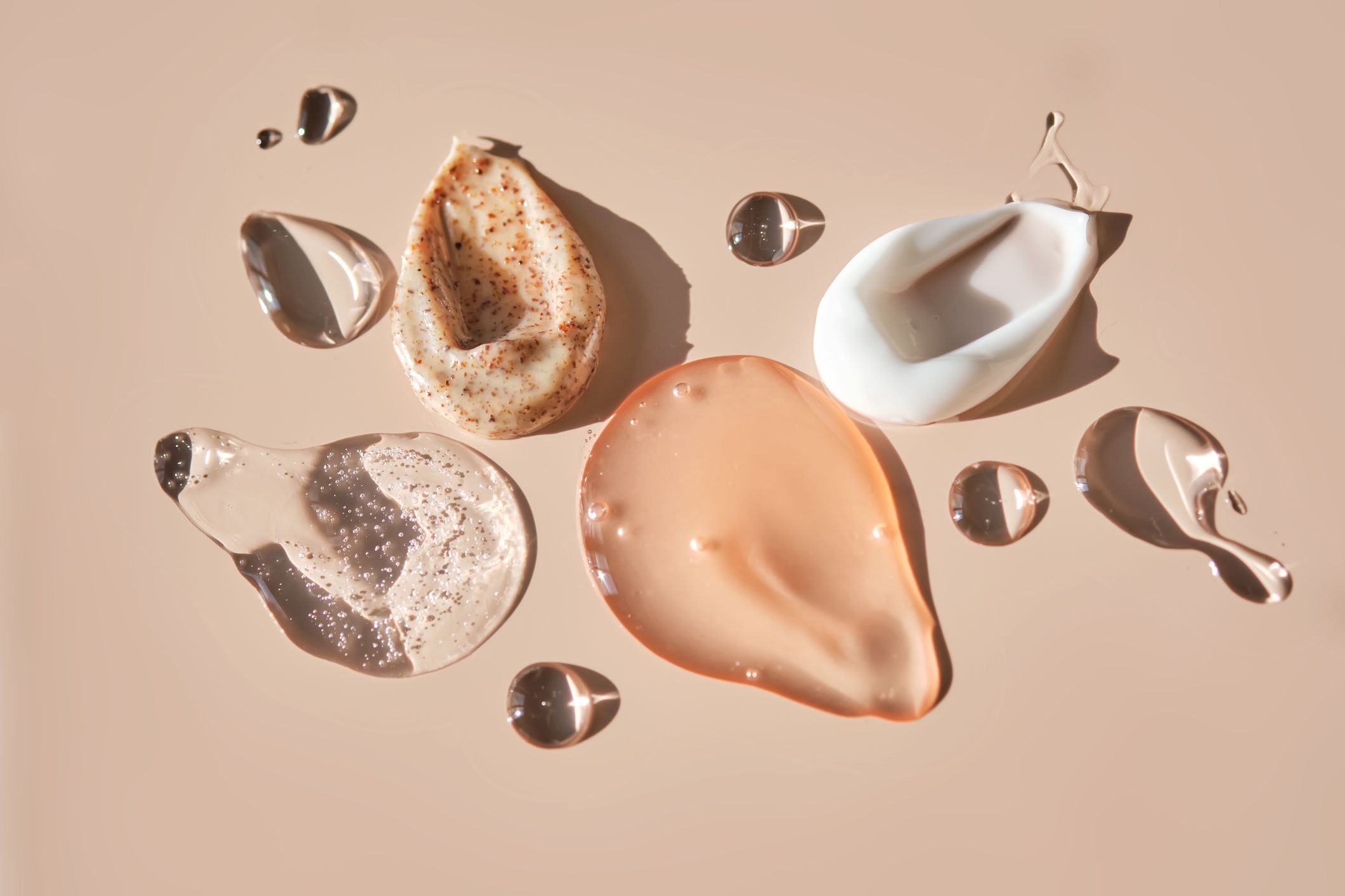 Ulike hudpleieprodukter i flytende og kremet konsistens arrangert på en lys bakgrunn.