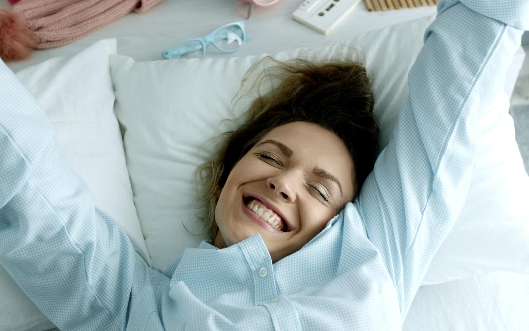 En kvinne ligger i en seng og strekker seg