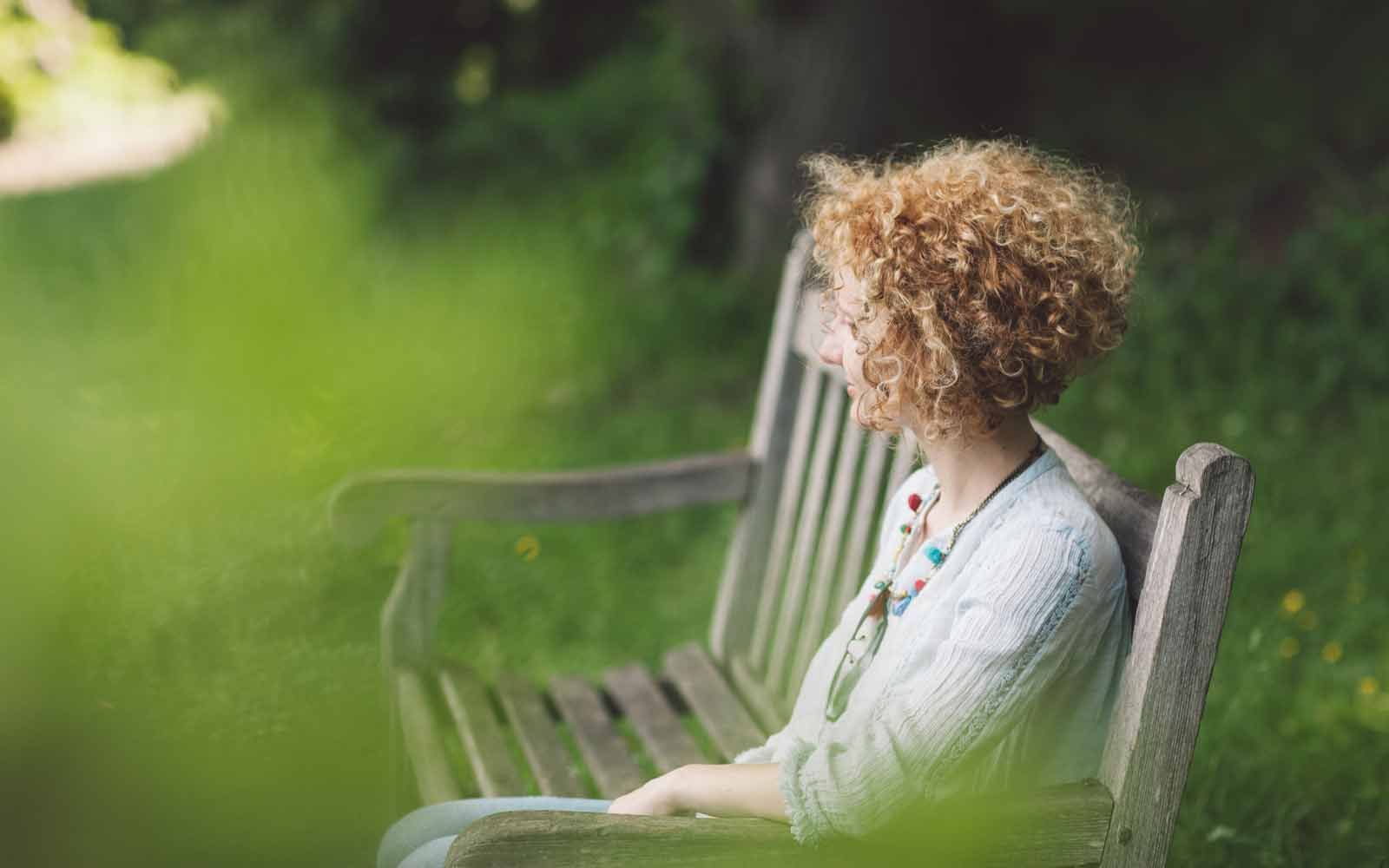 En kvinne med krøllete hår sitter på en park benk med ansiktet vendt bort fra kameraet
