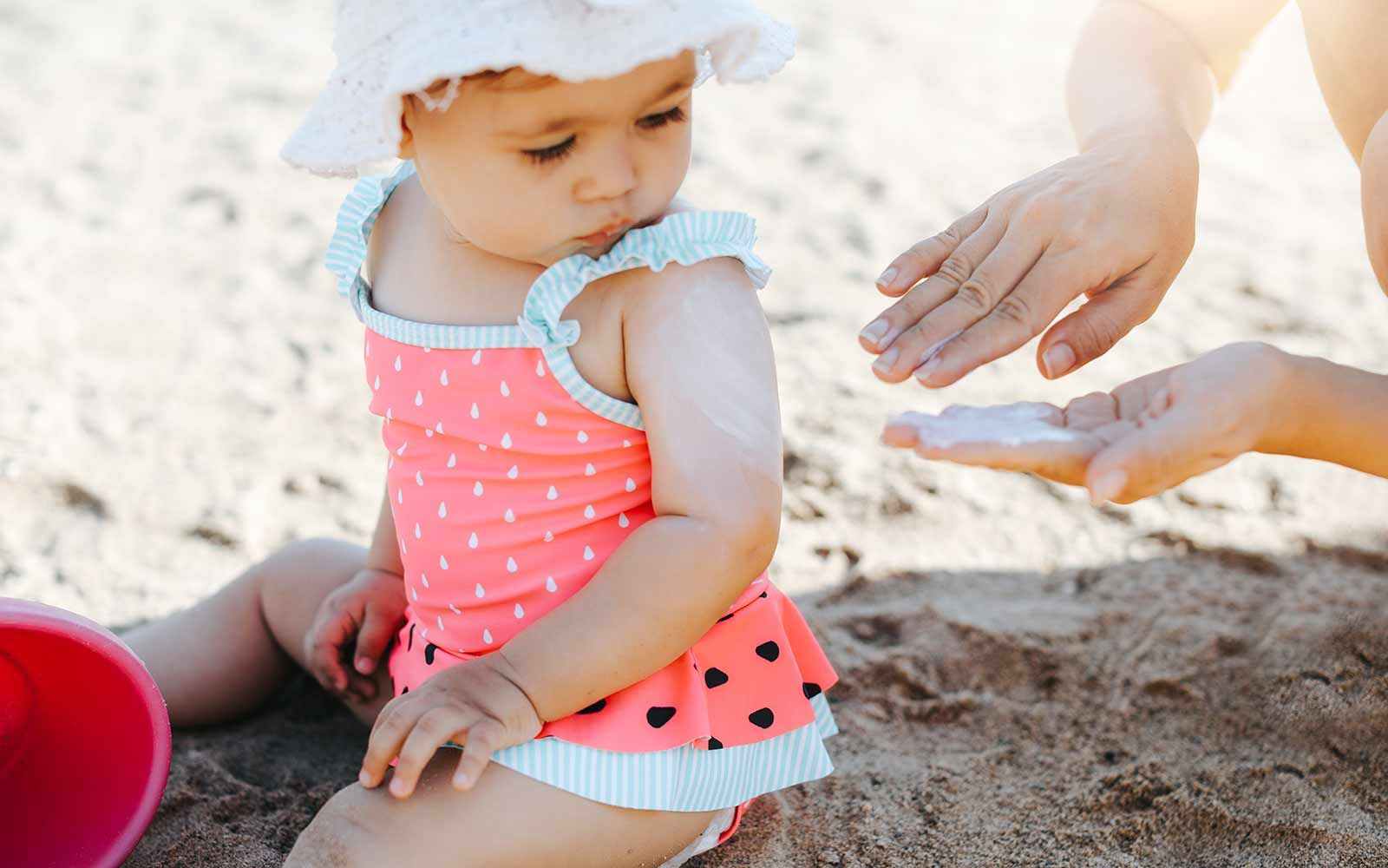 Barn på stranden blir smurt med solkrem