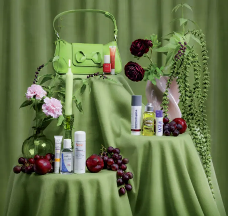 Bilde av en liten grønn veske på en pidestall med grønn duk. I forkant presenteres produkter som kan være nyttige på storbyferie.