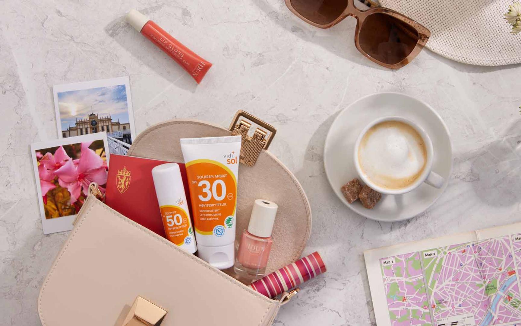 Liggende på bord veske, solkrem, leppepomade, neglelakk, solbriller, kart og kaffekopp – klar for sol og ferie.